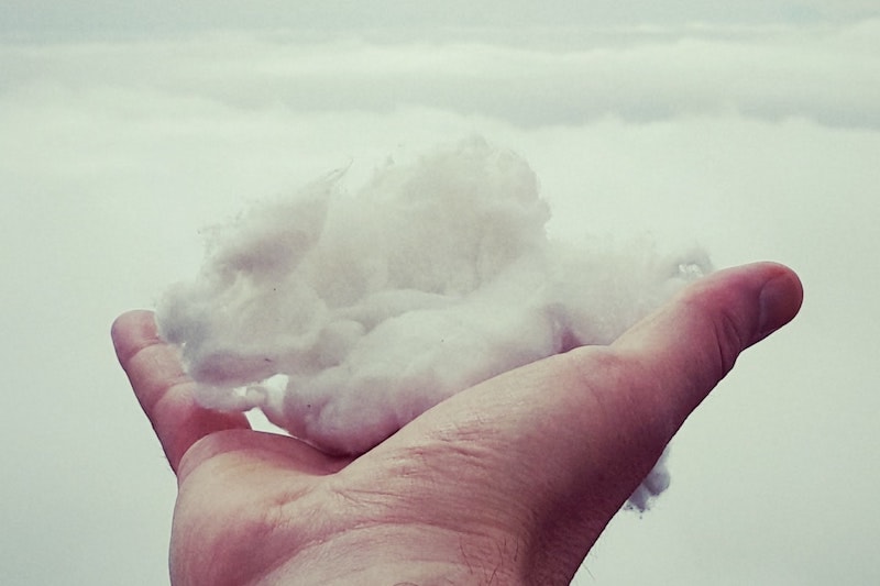 Henkilö pitää kädellään pilvenhattaraa muistuttavaa pumpulia pilvistä taustaa vasten.