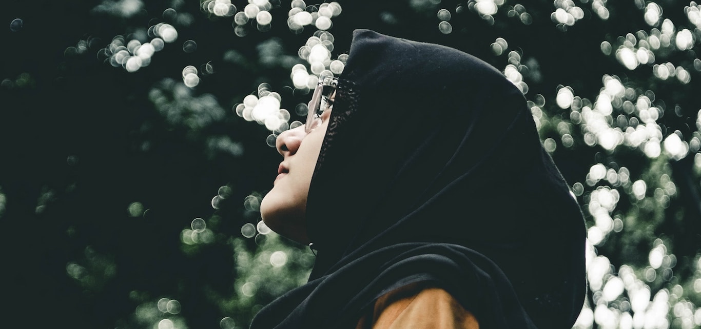 Nuori hijab-päinen musliminainen katsoo taustallaan puiden lehvästön vehreys.