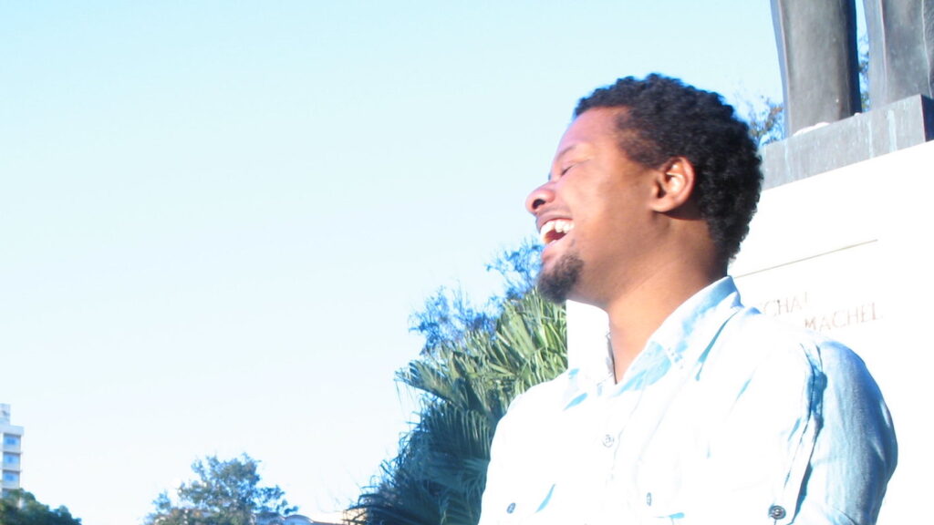 Rap-artisti Azagaia nauraa makeasti sinistä taivasta vasten.