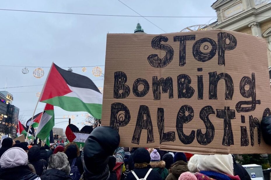 Mielenosoituskulkueessa palestiinan lippu ja teksti 'Stop bombing Palestine'.