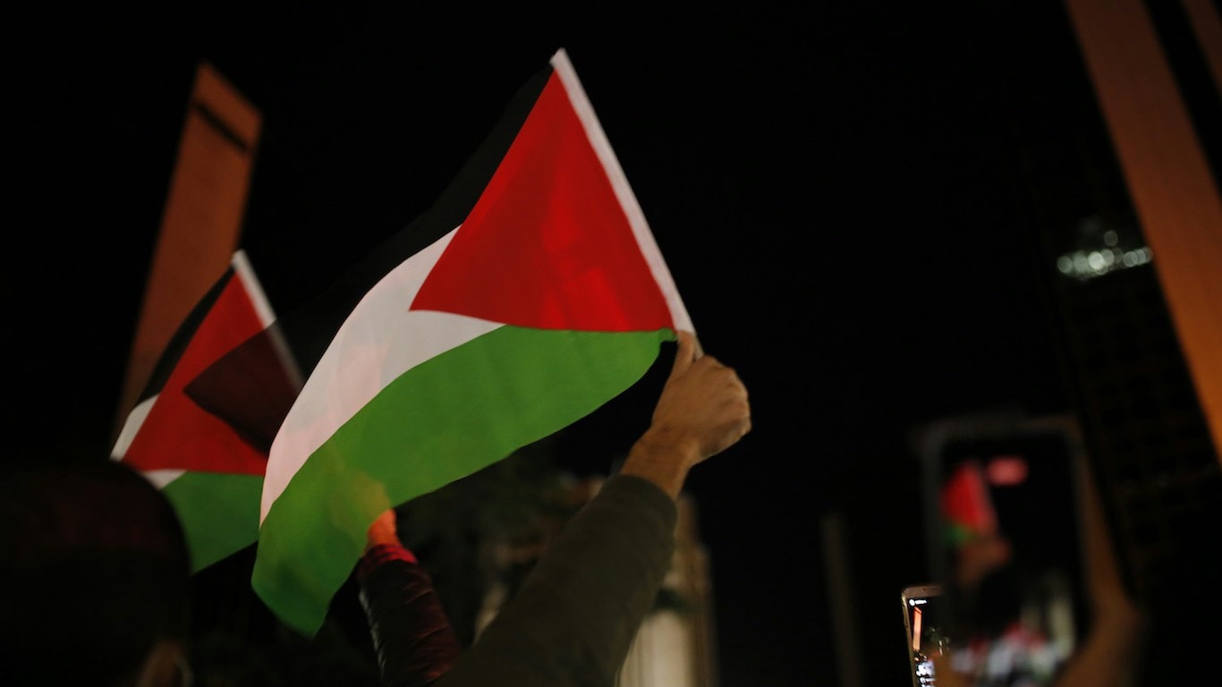 Palestiinan punavihervalkoinen lippu liehuu mielenosoittajan kädessä tummaa taustaa vasten.