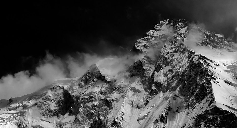 Mustavalkoinen kuva, jossa luminen ja terävähuippuinen vuori. Taivas on musta.